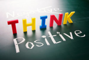 A sign saying negative think positive but the negative is crossed out.