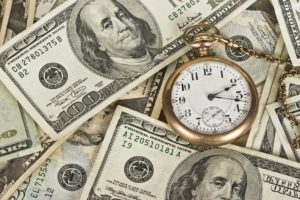 one hundred dollar notes spread out with a gold pocket watch laid on top.